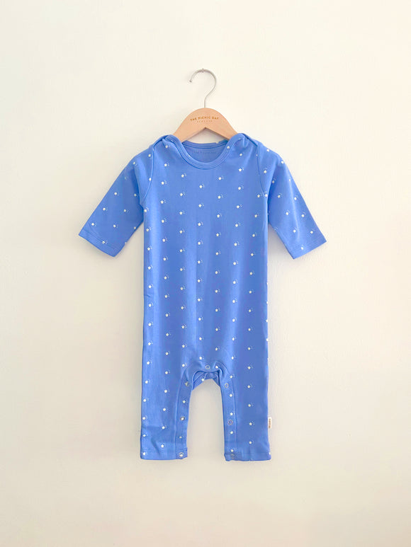 Blue baby onesie with white star pattern on a hanger against a beige background
