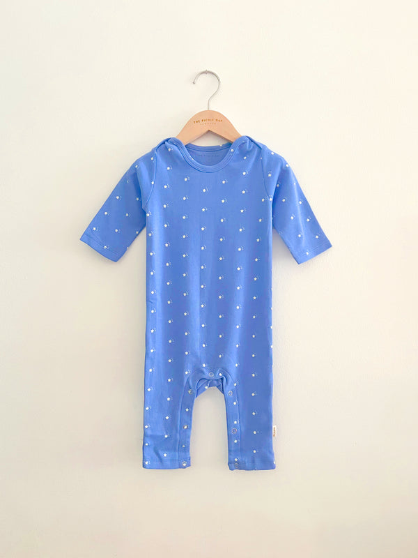 Blue baby onesie with white star pattern on a hanger against a beige background